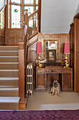 Pet dog sits under antique wooden desk in Arts and Crafts staircase of Haslemere home, Surrey, UK