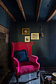 Bright pink armchair at fireside in muted blue room of Dartmoor farmhouse renovation Devon England UK