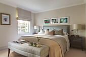 Framed prints above double bed with Roman blinds in window of London home UK