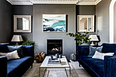 Square mirrors and seascape with deep blue velvet sofas at fireside in Clevedon living room Somerset, UK