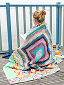 Woman sitting in crochet blanket reading a book rear view
