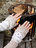 Woman warming hands at brazier with lace sleeve detail Brighton, East Sussex UK