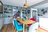Multicoloured chairs at dining table in open plan kitchen with light blue shelves Farnham home UK
