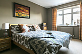 Gemusterte Bettdecke und Decke auf Holzbett mit Retro-Radio und Lampe in einem Haus in Farnham, Surrey, UK