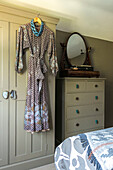 Vintage dress hangs with antique mirror on tallboy in Farnham bedroom Surrey UK
