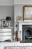 Lamp on chest of drawers with cello at fireside in Winchester home UK