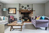Lilac sofa and cushions at exposed brick fireside with low wooden coffee table in Grade II listed Jacobean house Alton UK