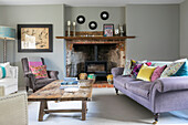 Lilac sofa and cushions at exposed brick fireside with low wooden coffee table in Grade II listed Jacobean house Alton UK