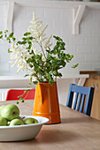 Cut flowers in range jug with apples on kitchen table
