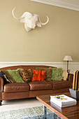Cushions on brown leather sofa with plaster cast of animal head