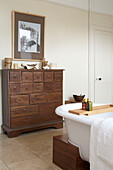 Antique chest in bathroom with freestanding roll-top bath and artwork