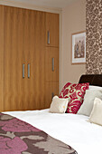 Floral patterned wallpaper and bed cover in London bedroom with fitted wardrobes