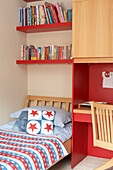 Single bed with star shaped cushion under bookshelves in child's room