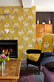 Wing-back armchair at lit fire with floral patterned wallpaper in Somerset home England UK