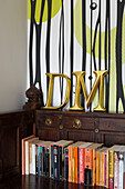 Letters D and M above book with patterned wallpaper in Coombe cottage, UK