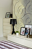Family photographs on sideboard in Coombe bedroom with spiral patterned wallpaper, England, UK