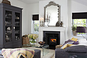 Mirror on mantlepiece above lit stove in Brook living room with grey painted cabinet, Isle of Wight, UK
