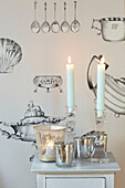 Lit candles and silverware with homeware patterned wallpaper in Kent home, England, UK