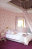Single bed with pink floral patterned wallpaper and ladder to mezzanine in Kent home, England, UK