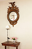 Gilt-framed convex mirror above wooden side table in hallway of semi-detached home UK