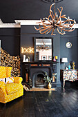 Gelber Sessel mit Kaminholz im schwarzen Wohnzimmer eines Stadthauses in Hastings, East Sussex, England UK