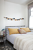 yellow linen pillows on double bed with string of lanterns in Brighton home East Sussex UK