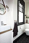 Black towels hang at frosted glass window with circular mirror above basin in bathroom of Brighton home East Sussex UK