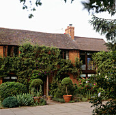 Außenansicht eines Hauses aus rotem Backstein mit Kletterpflanzen und Töpfen mit Buchsbaum zu beiden Seiten des Vordereingangs