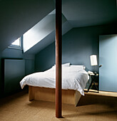 Schlafzimmer im Dachgeschoss mit Doppelbett in farbenfrohem Blau, Teppichfliesen und einem Velux-Fenster