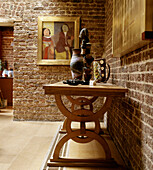 Table with a display of pots and sculpture in dining room with exposed brick wall and modern portrait painting