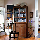 Cabinet with glass doors in dining room filled with plates beside open shelves with baskets and African sculpture