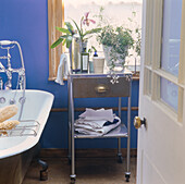 Blau gestrichenes Badezimmer mit Rolltop-Badewanne, Blumentöpfe mit Jasmin und Orchideen und Badeöle auf Vintage Metallschrank