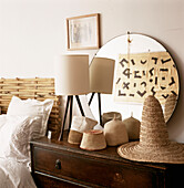 Schlafzimmerdetail mit afrikanischen Hüten auf einer Kommode, darüber runder Spiegel, in dem sich afrikanischer Textilwandbehang spiegelt