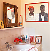 Nahaufnahme eines Waschbeckens mit Toilettenartikeln und einem alten Spiegel sowie einem afrikanischen Porträtgemälde an der Wand