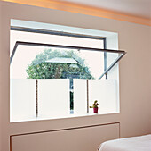 Open metal framed window in modern white panelled bedroom with frosted perspex screen and cactus
