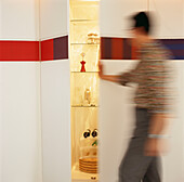Wand mit verdecktem Stauraum und bemaltem Fries, Mann öffnet die Tür zum beleuchteten Getränkeschrank