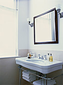 Nahaufnahme eines weißen Handwaschbeckens mit Toilettenartikeln und einem quadratischen Spiegel