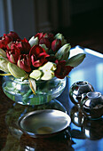 Glass bowl filled with tulips on a shiny table top with metal candle holders and dish