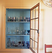 Built in cupboard with glass door painted in blue with assorted coloured glassware