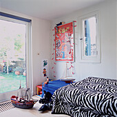 Zebra striped bedspread and toy galleon in boy's bedroom with garden views
