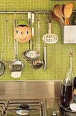 Close up of kitchen utensils on pale green mosaic tiles above stainless steel kitchen work-top
