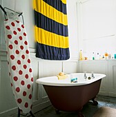 Pop Art still life of red and white polka dot ironing board and signalling flag in white panelled bathroom with roll top bath