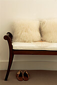 Dark wood bench seat in hallway with upholstered white cover and sheepskin cushions