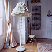 In Spitze und Rüschen gehüllter Lampenschirm auf einer Stehlampe in einem eleganten weiß getäfelten Salon