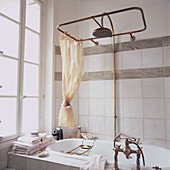 Old fashioned shower above roll top bath in tiled bathroom