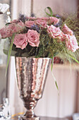 Close up of a bouquet of pink roses with blue flowers in silvered glass vase