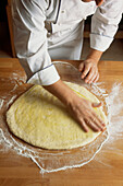 Chef rolling out dough on a floured surface in a kitchen