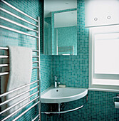 Corner wash hand basin with heated towel rail in modern bathroom tiled in turquoise green mosaics