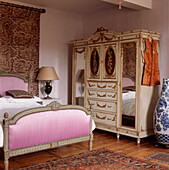 Ornate French period style bedroom with pink velvet fabric covered bedstead and decorative gold leaf wardrobe