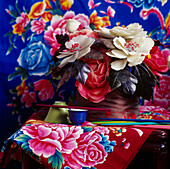 Still life of brightly coloured Chinese fabrics behind handmade Mexican wax flowers and other Chinese artifacts
